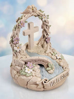 Decorative figurine with cross, flowers, and 'He Is Risen' text against a blurred background